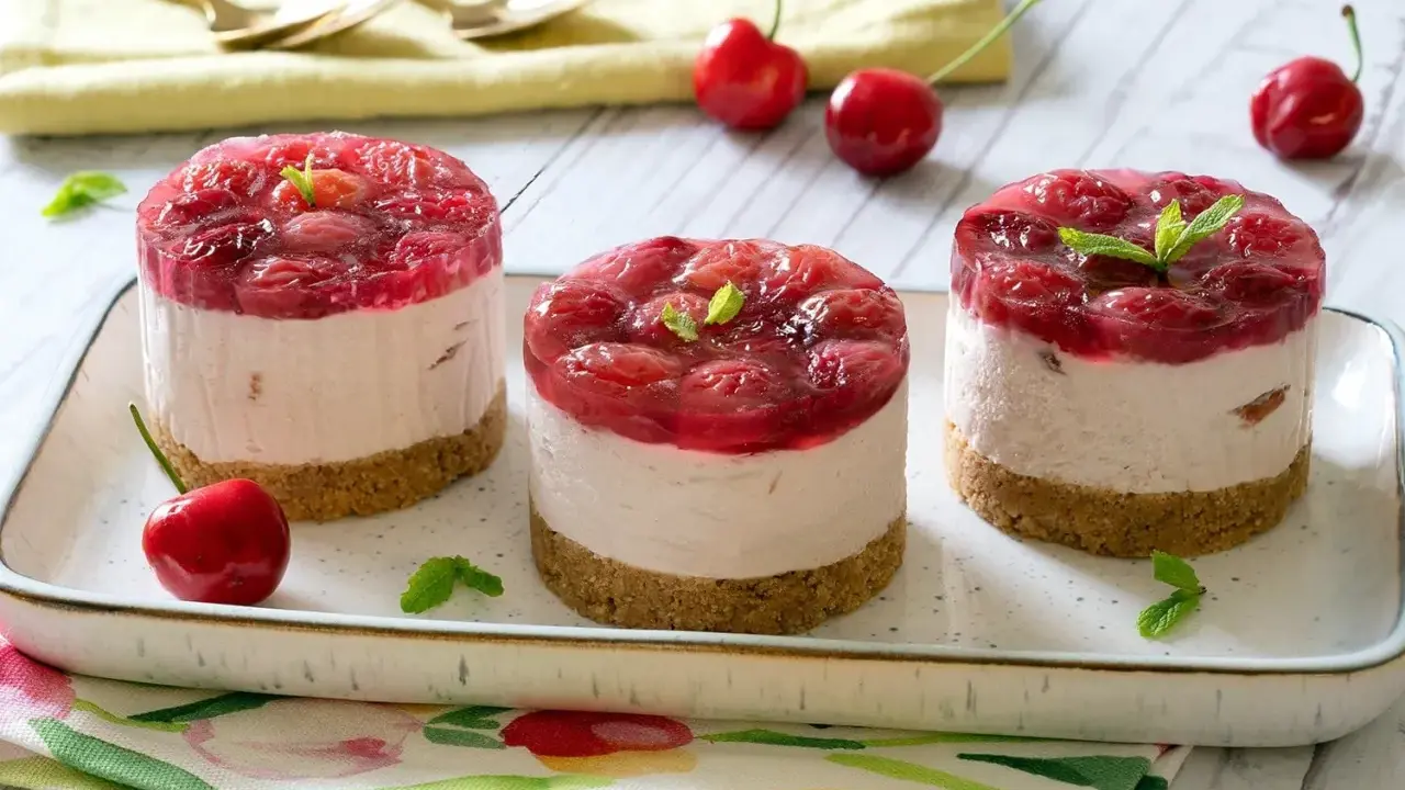 Three mini cheesecakes with cherry topping on a platter, garnished with mint leaves and fresh cherries.