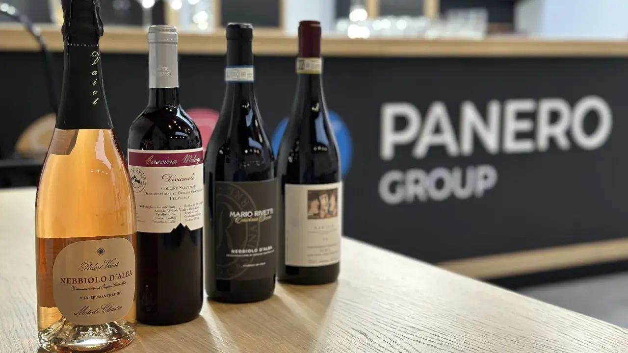 Four bottles of wine, including a rosé sparkling wine, on a wooden table with a blurred background.