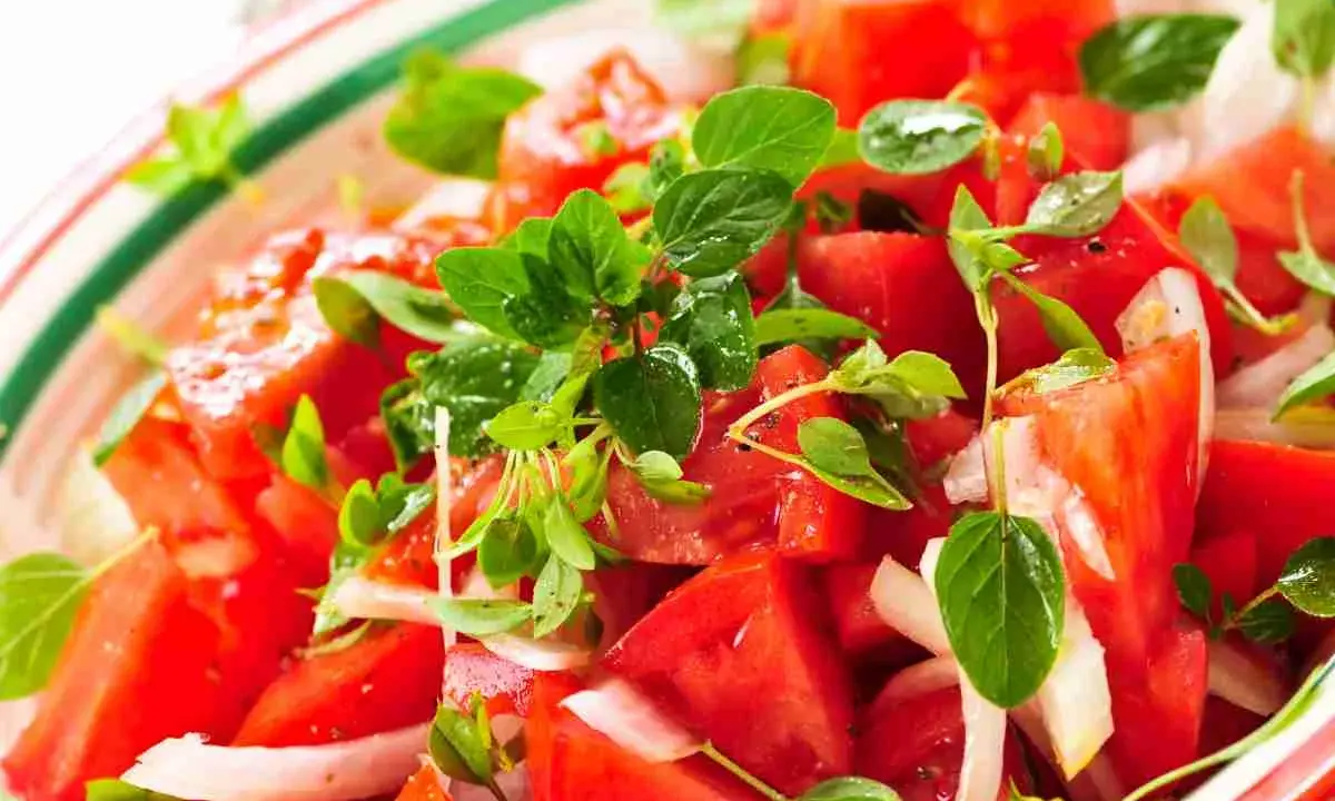 Close-up of a fresh tomato salad with basil and onion in a colorful bowl.