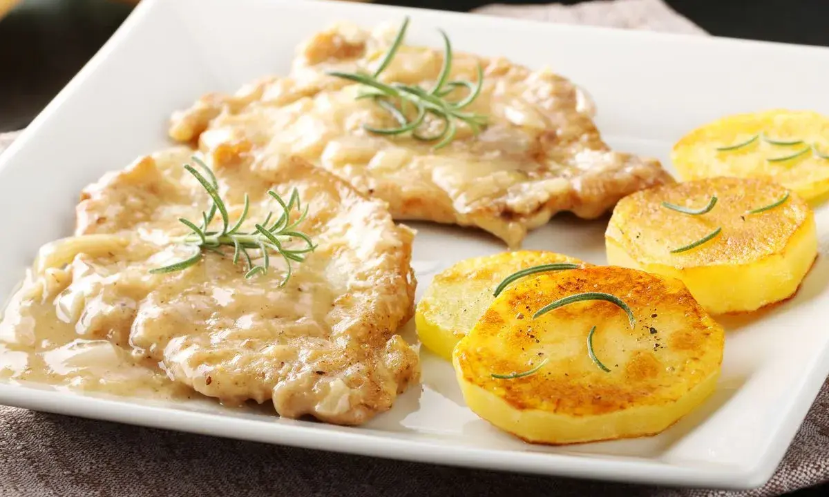 Two breaded cutlets in creamy sauce with rosemary, served with pan-fried potato slices.