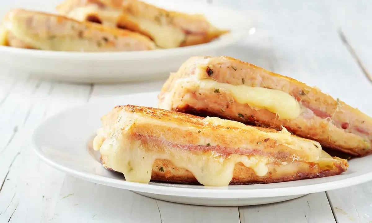 Two grilled sandwiches with melted cheese on white plates.