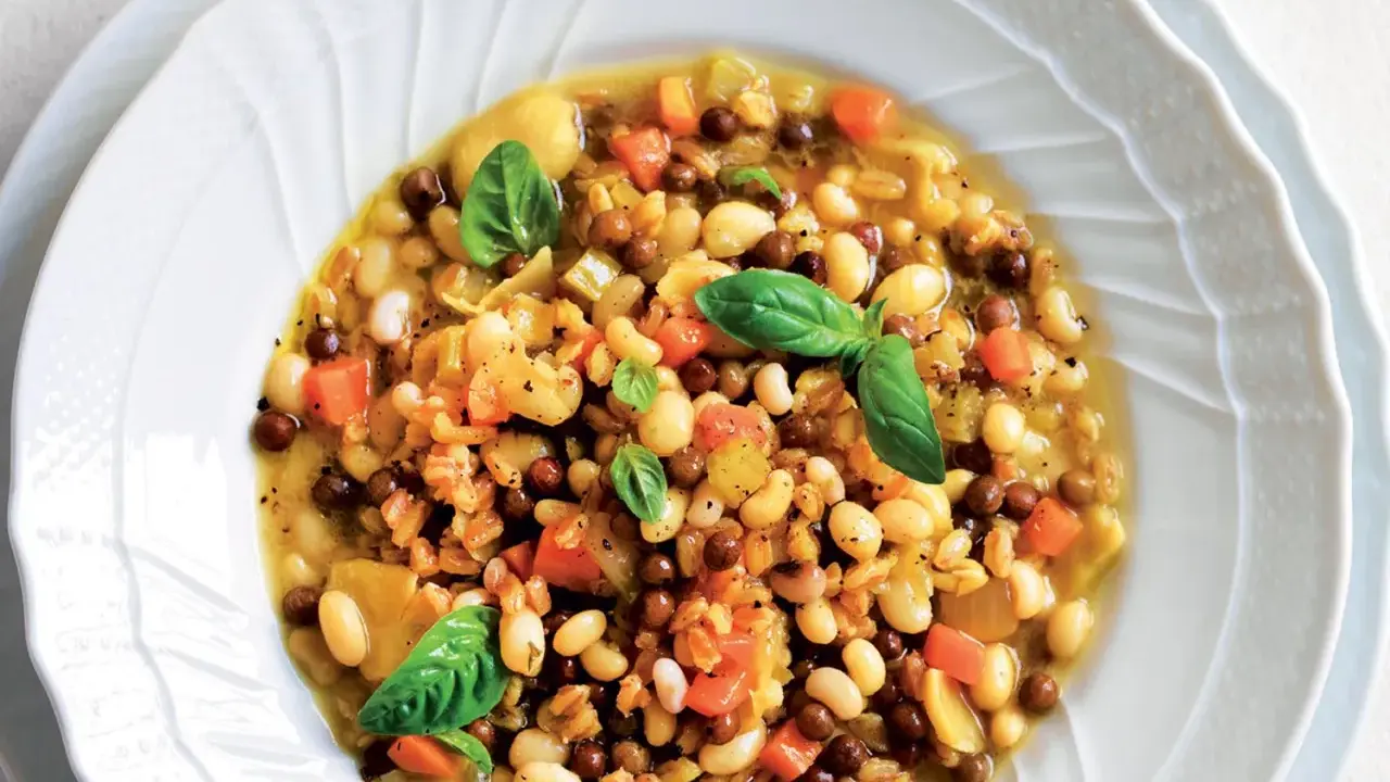 A hearty bowl of farro soup with white beans, lentils, carrots, and basil.