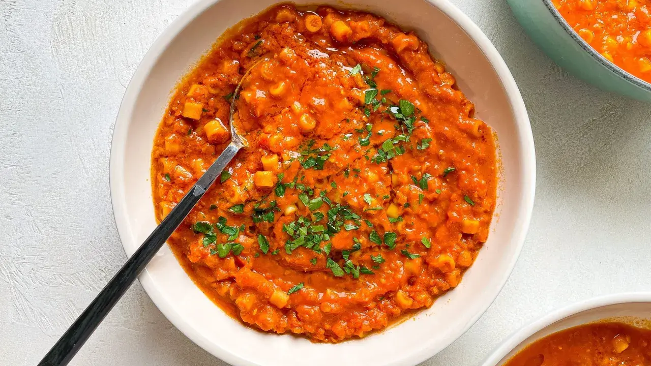 A bowl of creamy red lentil soup with small pasta and parsley, with a spoon.