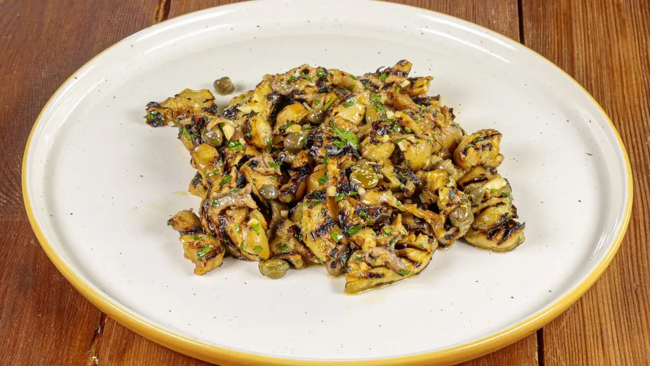 Grilled eggplant salad with capers and herbs on a white plate.