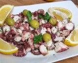 Octopus salad with olives, parsley, and lemon wedges on a white plate.
