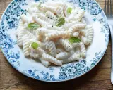 Fusilli pasta with a creamy white sauce, garnished with mint leaves, on a blue and white floral plate.