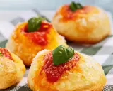 Four small, round Italian pastries topped with tomato sauce, grated cheese, and fresh basil leaves on a checkered cloth.