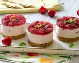 Three mini cheesecakes with cherry topping on a platter, garnished with mint leaves and fresh cherries.