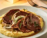 Sliced beef in sauce with onions and rosemary on a bed of polenta.
