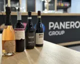 Four bottles of wine, including a rosé sparkling wine, on a wooden table with a blurred background.