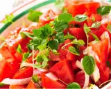 Close-up of a fresh tomato salad with basil and onion in a colorful bowl.