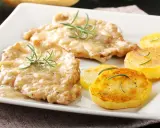 Two breaded cutlets in creamy sauce with rosemary, served with pan-fried potato slices.