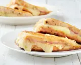 Two grilled sandwiches with melted cheese on white plates.