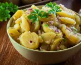 A bowl of German potato salad with red onion and parsley.