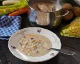 A bowl of hearty barley soup with vegetables and beans, next to a pot of soup and fresh ingredients.