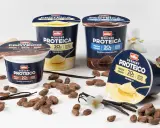 Müller protein desserts in chocolate and vanilla flavors, with cocoa beans, vanilla pods, and a scoop of cocoa powder.