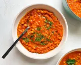 A bowl of creamy red lentil soup with small pasta and parsley, with a spoon.