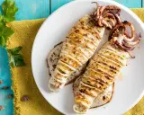 Two grilled calamari on a white plate, seasoned with herbs, on a blue wooden table.
