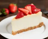 Slice of cheesecake topped with fresh strawberries on a white plate.