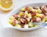 Octopus and potato salad with lemon and parsley in a white bowl.