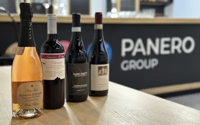 Four bottles of wine, including a rosé sparkling wine, on a wooden table with a blurred background.