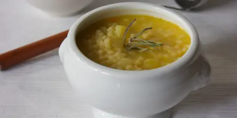 A white bowl of creamy potato soup with small pasta and a sprig of rosemary.