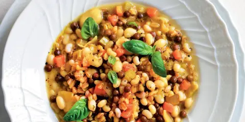 A hearty bowl of farro soup with white beans, lentils, carrots, and basil.