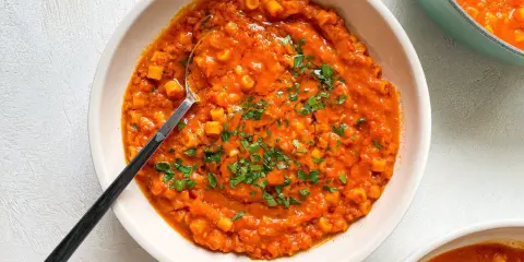 A bowl of creamy red lentil soup with small pasta and parsley, with a spoon.