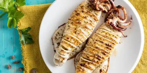 Two grilled calamari on a white plate, seasoned with herbs, on a blue wooden table.