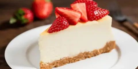 Slice of cheesecake topped with fresh strawberries on a white plate.