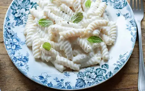 Fusilli pasta with a creamy white sauce, garnished with mint leaves, on a blue and white floral plate.