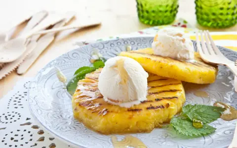 Grilled pineapple slices topped with scoops of vanilla ice cream and drizzled with honey.