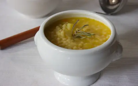 A white bowl of creamy potato soup with small pasta and a sprig of rosemary.