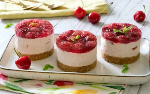 Three mini cheesecakes with cherry topping on a platter, garnished with mint leaves and fresh cherries.
