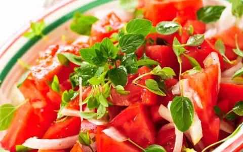 Close-up of a fresh tomato salad with basil and onion in a colorful bowl.