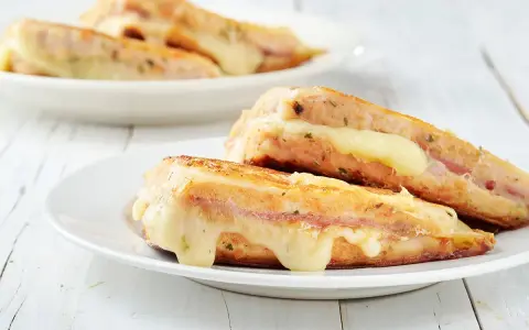 Two grilled sandwiches with melted cheese on white plates.