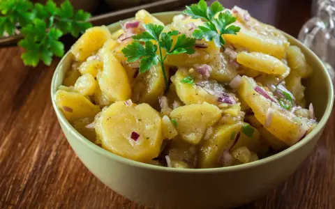 A bowl of German potato salad with red onion and parsley.