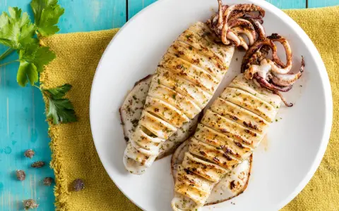 Two grilled calamari on a white plate, seasoned with herbs, on a blue wooden table.