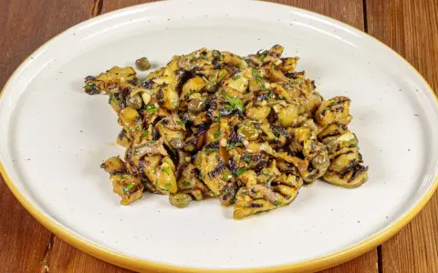 Grilled eggplant salad with capers and herbs on a white plate.
