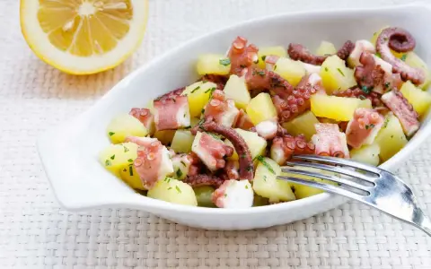 Octopus and potato salad with lemon and parsley in a white bowl.