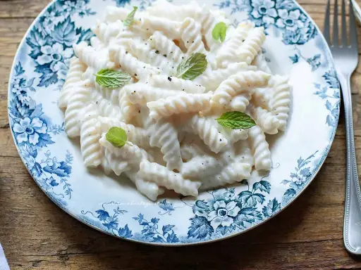 Fusilli pasta with a creamy white sauce, garnished with mint leaves, on a blue and white floral plate.
