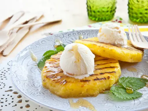 Grilled pineapple slices topped with scoops of vanilla ice cream and drizzled with honey.