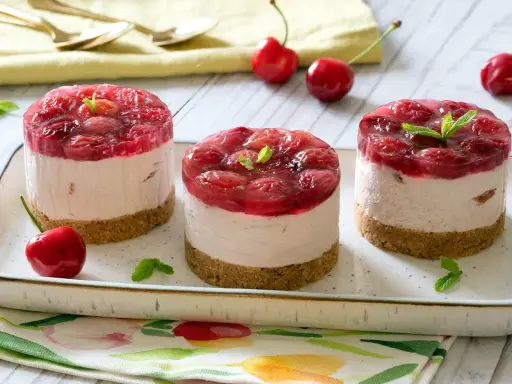 Three mini cheesecakes with cherry topping on a platter, garnished with mint leaves and fresh cherries.