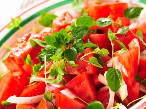 Close-up of a fresh tomato salad with basil and onion in a colorful bowl.