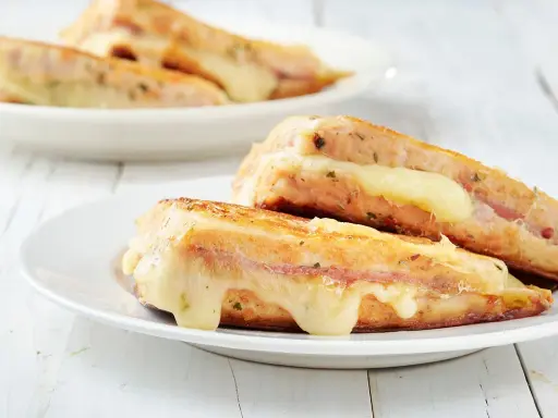 Two grilled sandwiches with melted cheese on white plates.