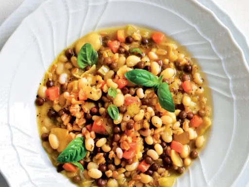 A hearty bowl of farro soup with white beans, lentils, carrots, and basil.