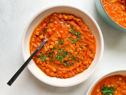 A bowl of creamy red lentil soup with small pasta and parsley, with a spoon.