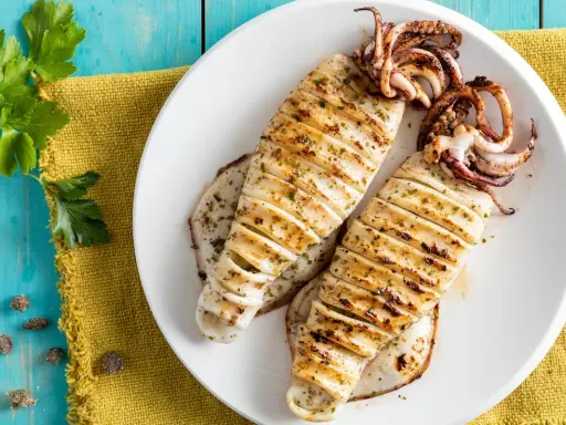 Two grilled calamari on a white plate, seasoned with herbs, on a blue wooden table.