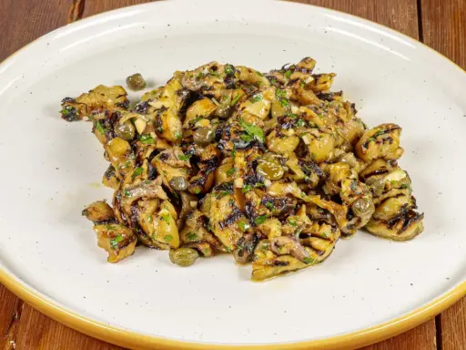 Grilled eggplant salad with capers and herbs on a white plate.