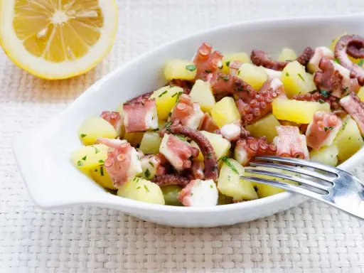 Octopus and potato salad with lemon and parsley in a white bowl.